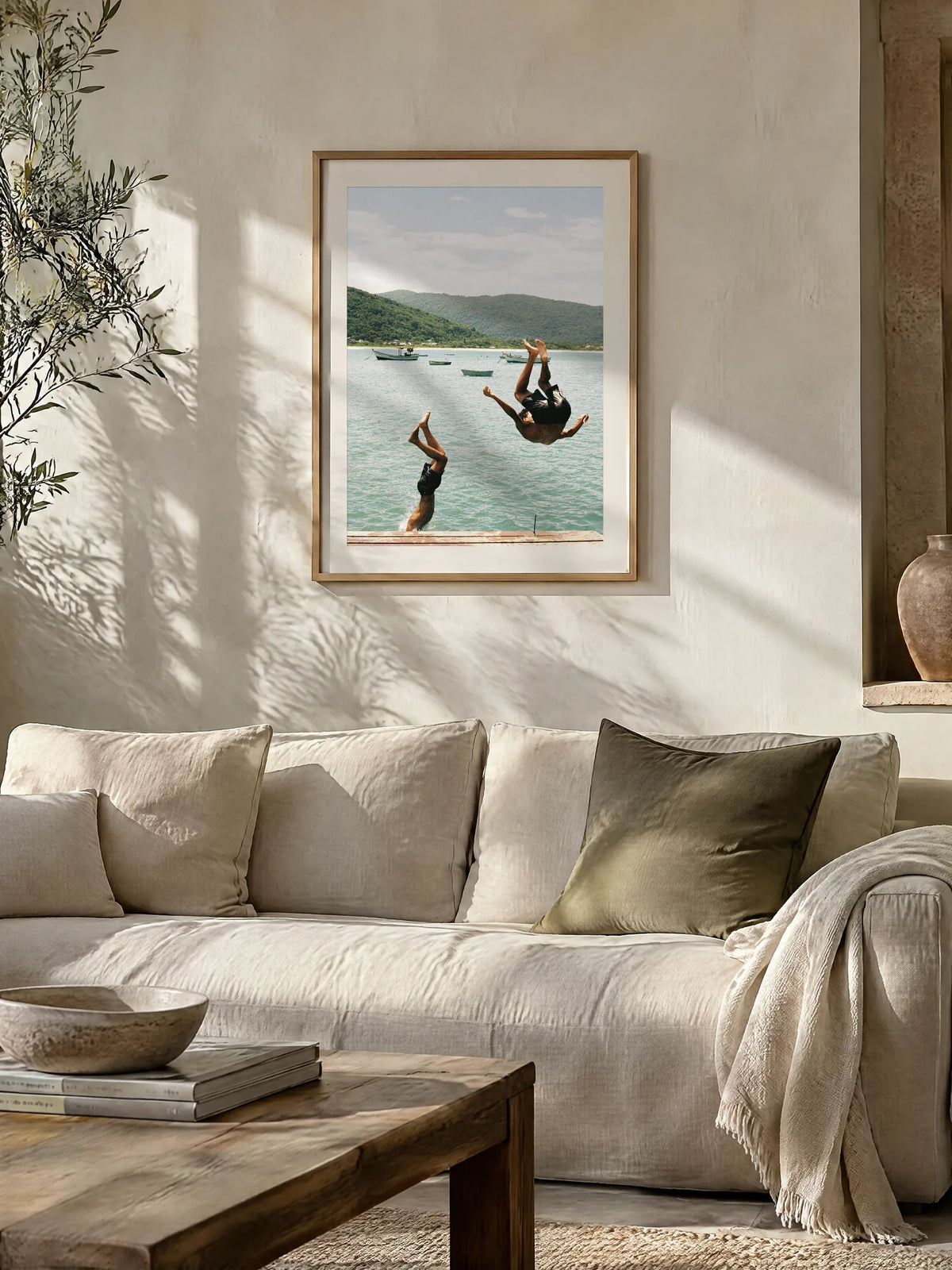 Into the Water by Laís Tomaselli, framed in natural oak with a white mat (24 × 32 in), above a sofa in a sunlit Mediterranean living room