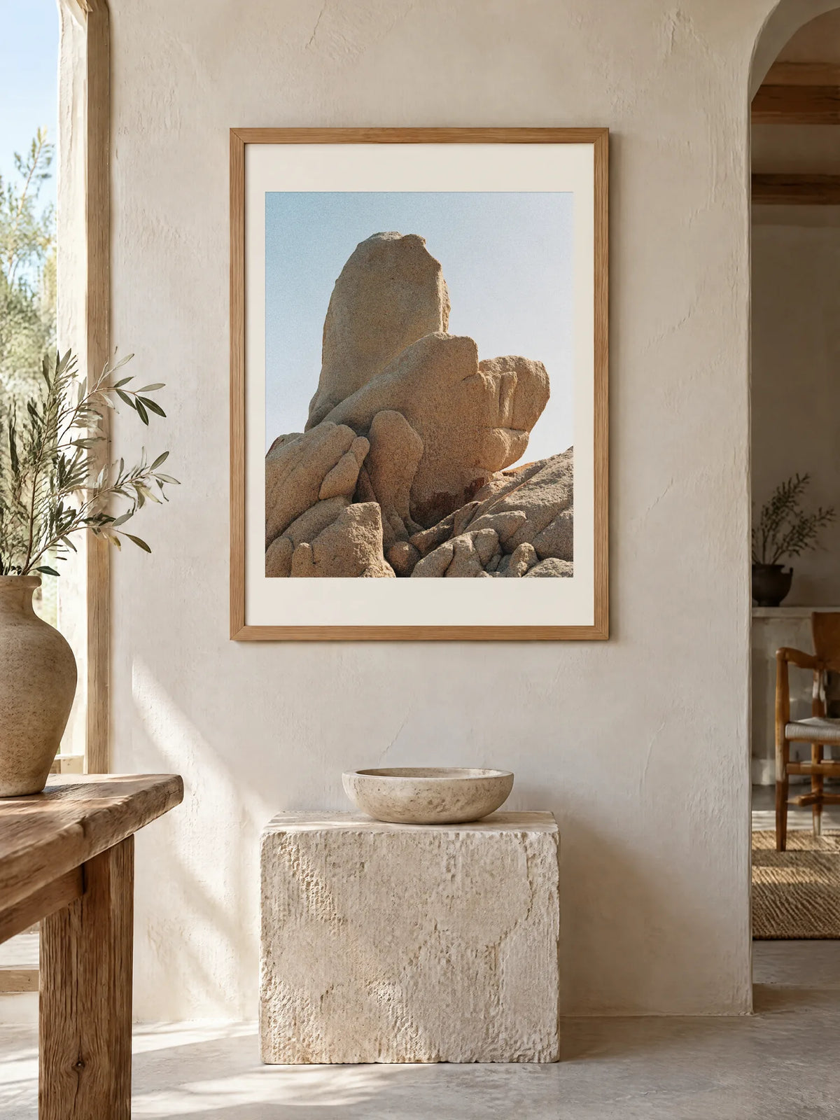Rock Forms by Laís Tomaselli, framed in natural oak with a white mat (18 × 24 in), above a stone plinth in a lime-plastered room