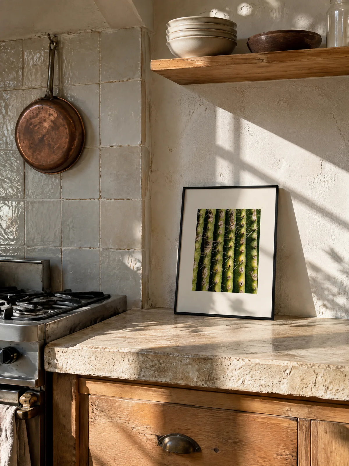Cactus by Laís Tomaselli, framed in black metal with a white mat (12 × 16 in), leaning on a stone kitchen counter