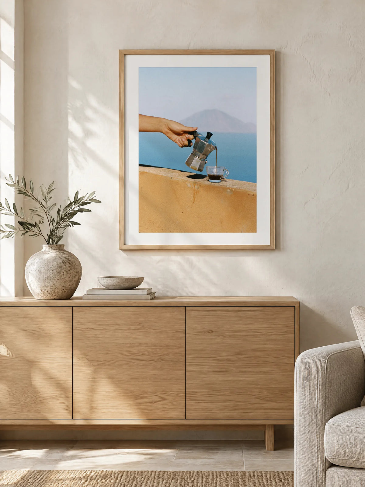 Morning Coffee by Wam Ornelas, framed in natural oak with a white mat (24 × 32 in), above an oak sideboard